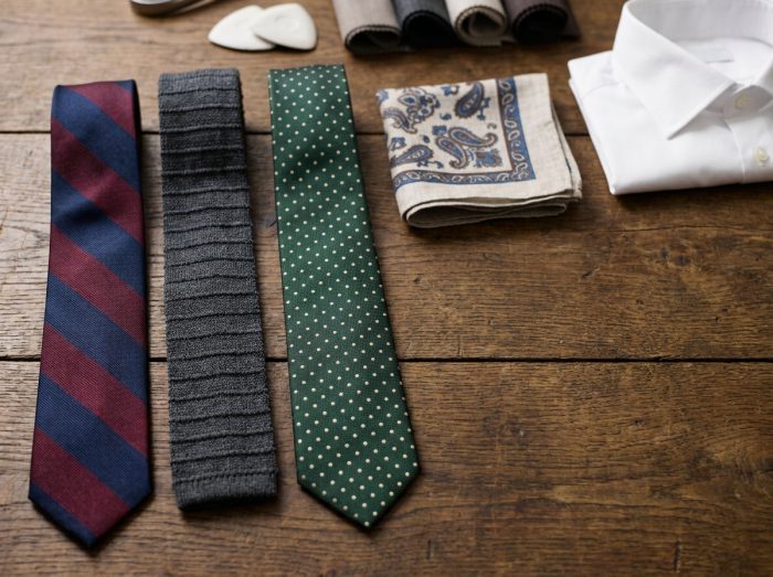 Trois cravates aux motifs variés disposées en flat lay sur une table en bois avec un carré de poche, guide visuel pour assortir sa cravate
