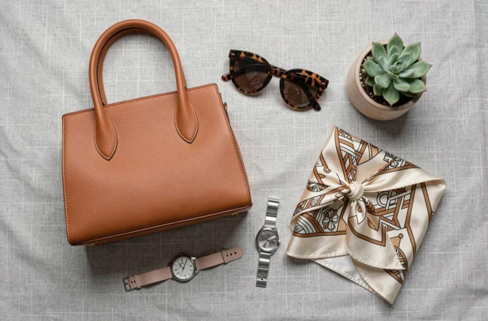 Flat lay tendance avec accessoires de mode incontournables de la saison : sac en cuir, lunettes, foulard soie et montre minimaliste